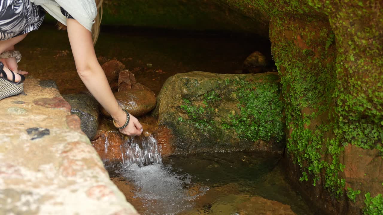 una chica lavando las manos en un refrescante manantial de montaña de una roca