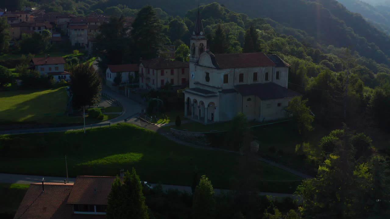Veduta aerea della suggestiva chiesa parrocchiale di un villaggio italiano situata accanto a colline boscose ad Arola, Italia