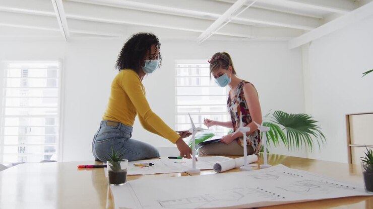 Two woman wearing face mask discussing over documents on table at office