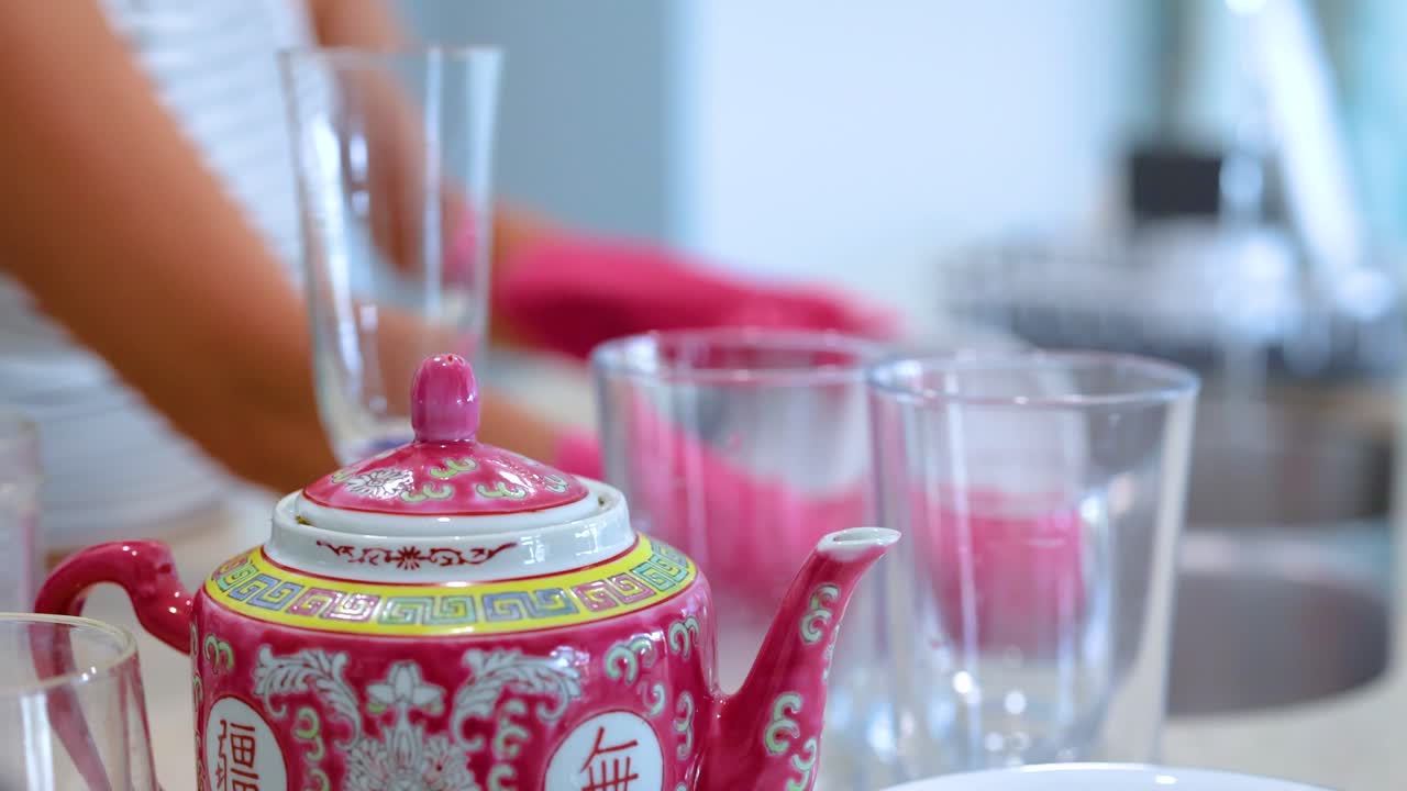 Hands wash dishes and glassware in a well-lit kitchen with vibrant decor and a focus on cleanliness