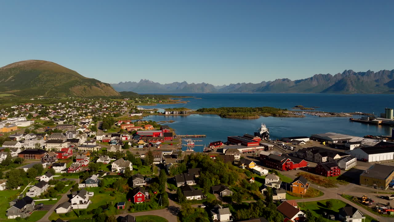 Aerial drone footage of Melbu town in Hadsel Municipality. Features colorful houses, the harbor, and majestic mountains of the Lofoten archipelago in Northern Norway on a sunny day
