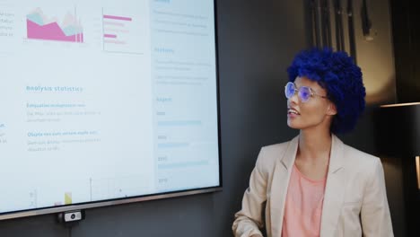 biracial casual businesswoman with blue afro making presentation in office, slow motion