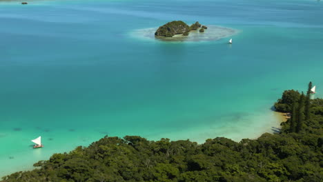 Pirogue-outrigger-sailboats-transport-tourists-to-explore-uninhabited-islands-in-Upi-Bay,-Isle-of-Pines---aerial-flyover