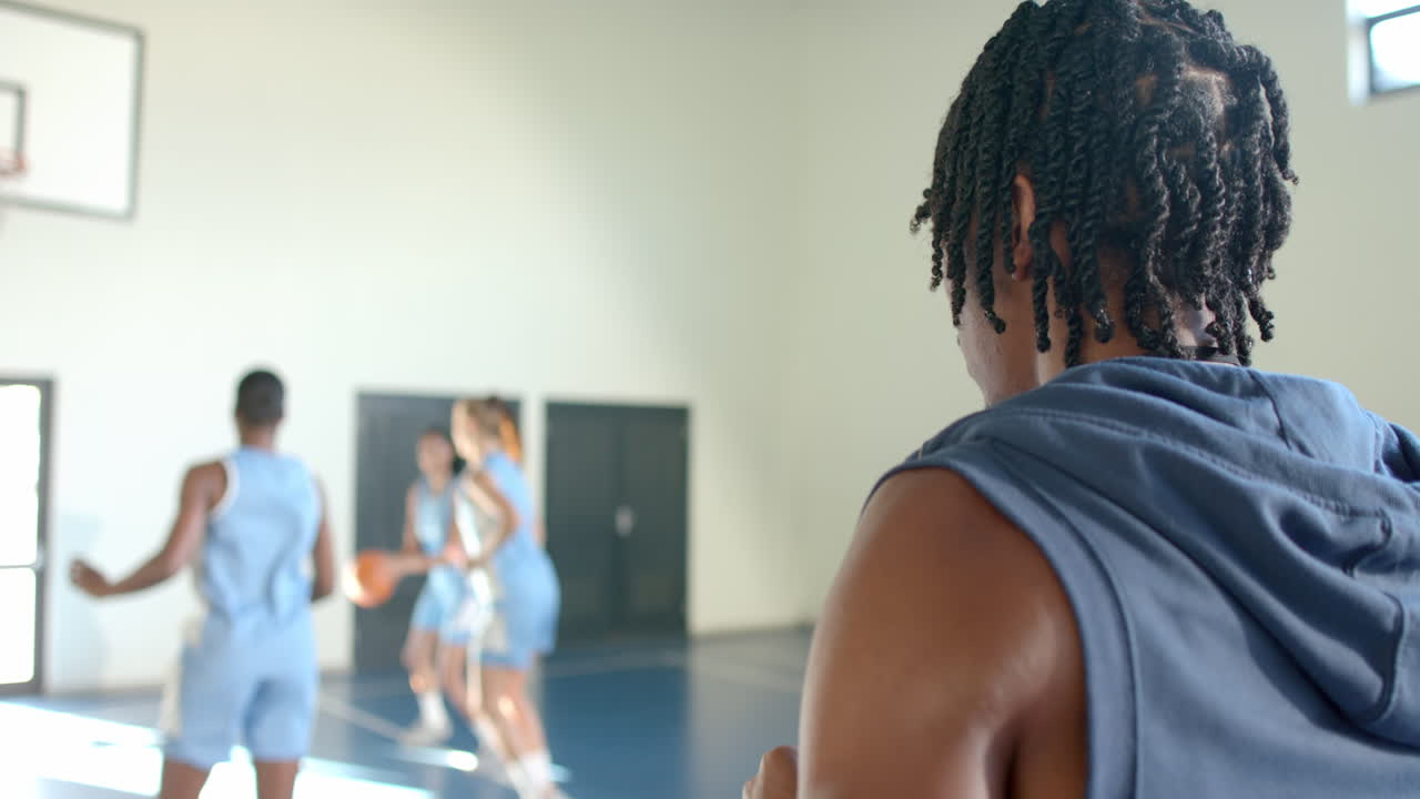 Drinking water, female basketball player watching teammates practice on court, copy space