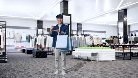 full view of an asian shopping man with a white card and shopping bags smile to camera while standing in clothing store