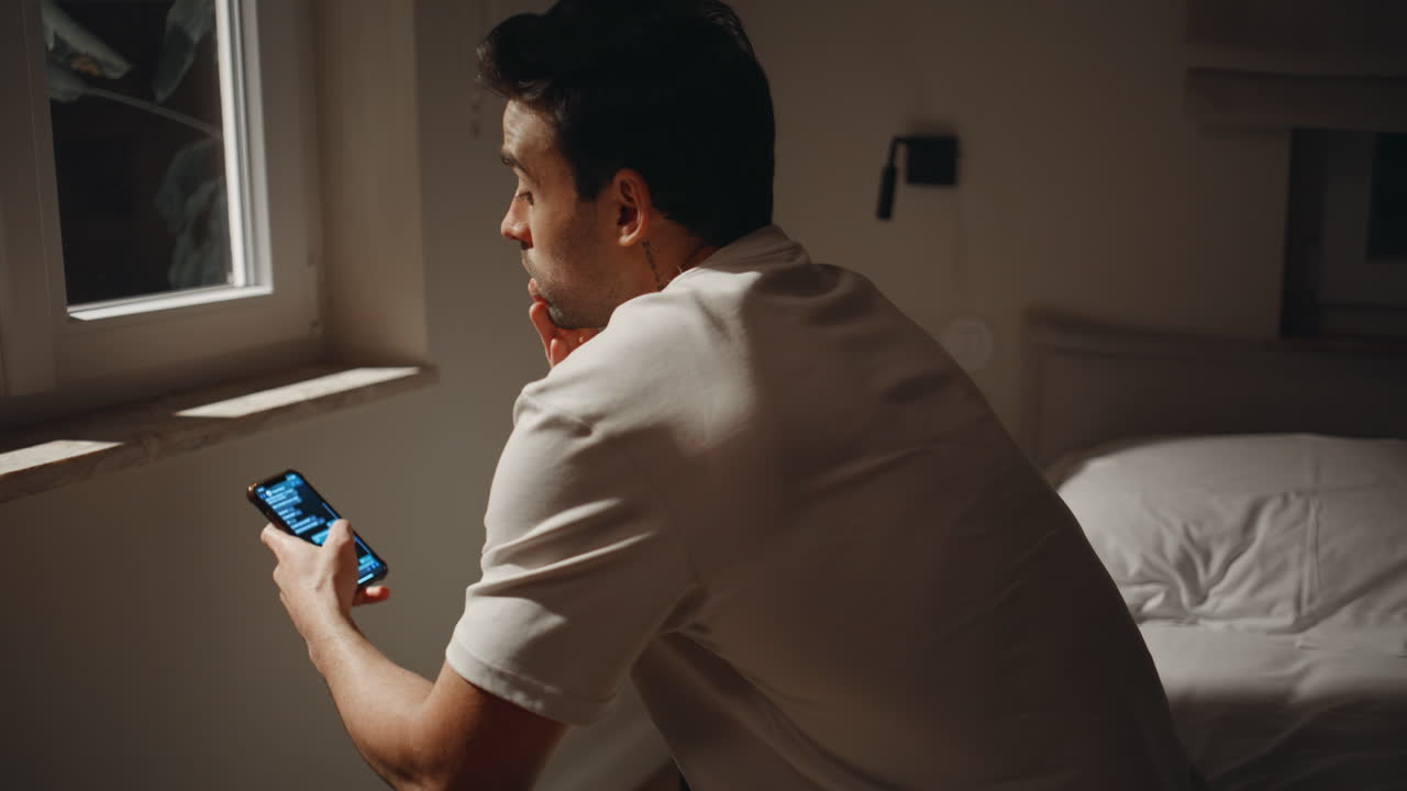 Night guy looking cellphone sitting home bed by window. Sleepless man texting