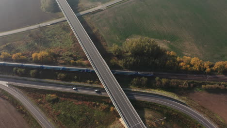 Train-passing-under-a-freeway-bridge-intersection---Aerial-top-view,-Europe