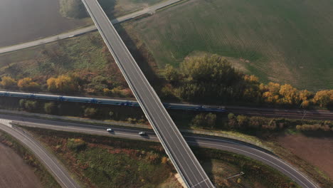 train passing under a freeway bridge intersection - aerial top view, europe