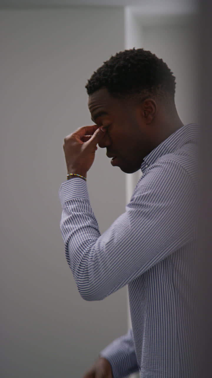 video vertical de un joven empresario en la oficina mirando un mensaje con malas noticias en el teléfono móvil y apoyado contra la pared pareciendo infeliz y deprimido 2