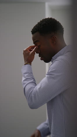 vertical video of young businessman in office looking at message with bad news on mobile phone and leaning against wall looking unhappy and depressed 2