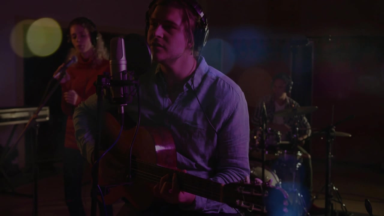 Band che si accorda in uno studio musicale, strimpellando accordi, armonizzando e accentuando la batteria sotto un bokeh viola.