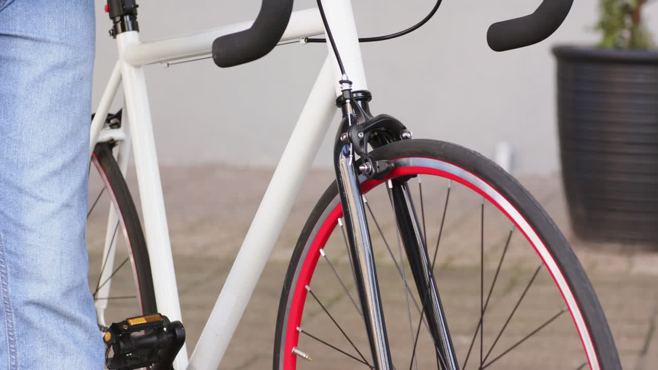 Persona che appare dal bordo sinistro e spinge una bicicletta bianca lungo il patio pavimentato verso una panchina per riposare