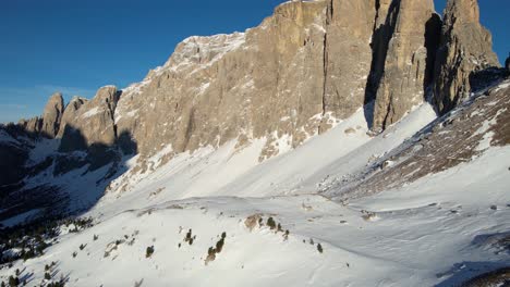 Vista-Aérea-De-Acantilados-Escarpados-En-Los-Dolomitas-Italianos-Sobre-Colinas-Cubiertas-De-Nieve-En-El-Soleado-Día-De-Primavera,-Disparo-De-Drones