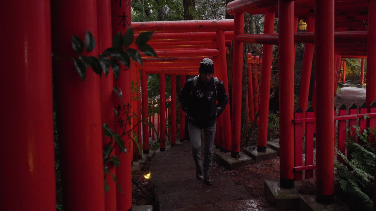 Young man walking up through multiple Torii gates in winter, Kanazawa, Japan