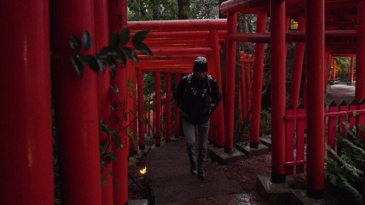 Giovane uomo che sale attraverso diversi cancelli Torii in inverno, Kanazawa, Giappone