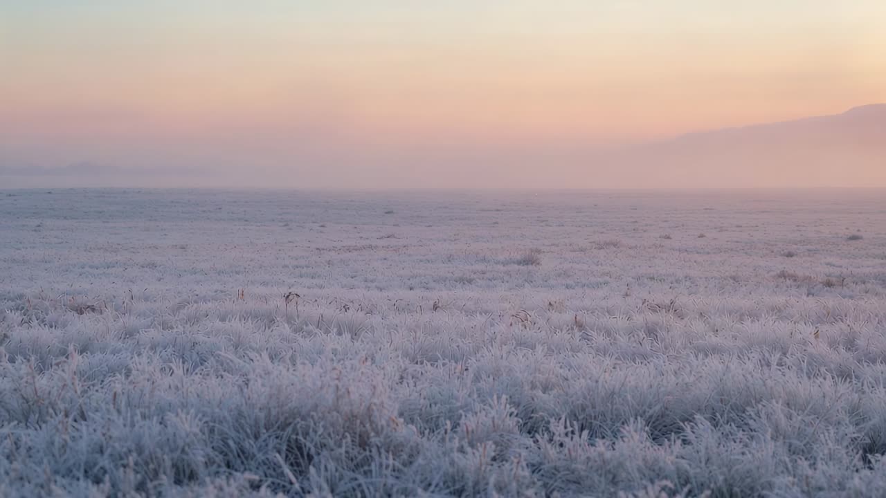 Sunrise bathing frost-covered plain revealing pastel sky at dawn, with thin mist and distant ridge