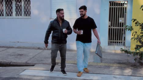 two men walking and talking on a city sidewalk with coffee