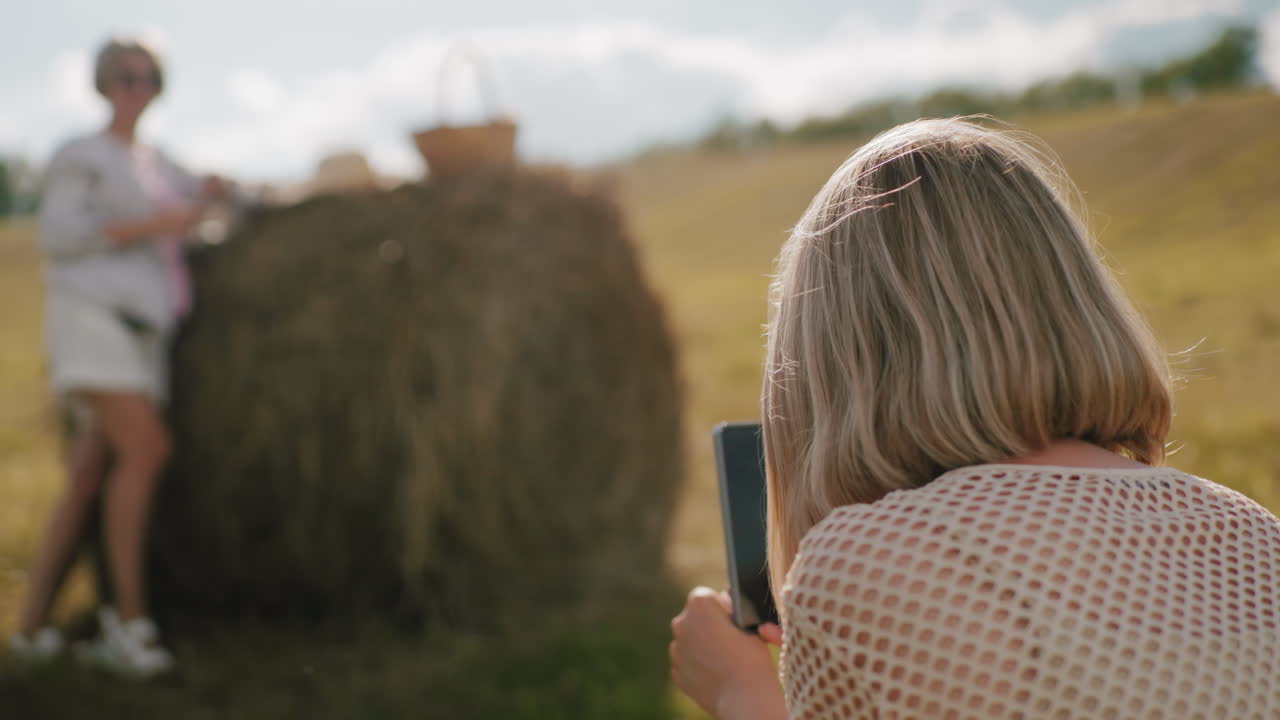 황금빛의 빛으로 광활한 농지에서 그녀의 여동생의 사진을 찍는 여자의 뒷면,  어리와 피크닉 바구니와 함께 경치 좋은 시골 설정은 따뜻한 시골 분위기를 만니다.