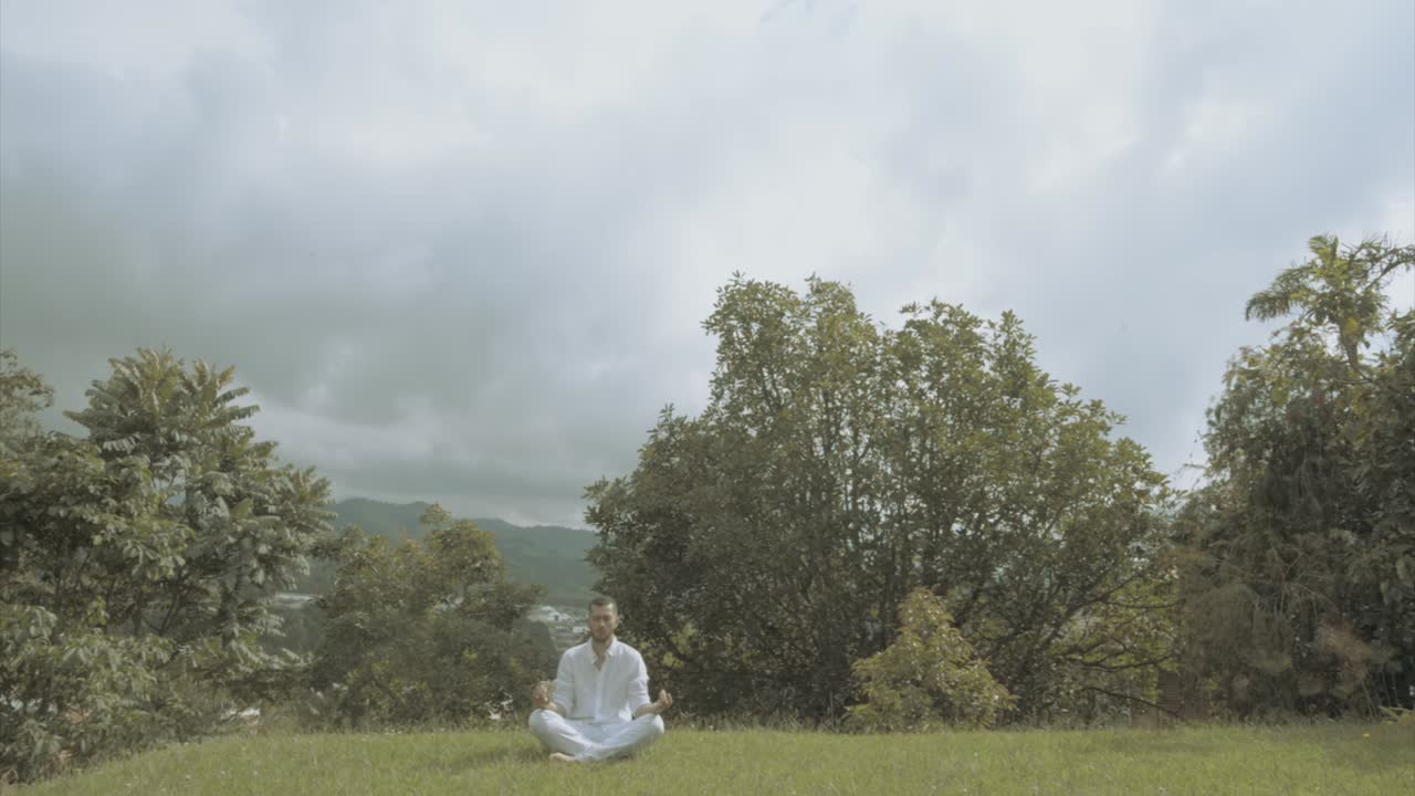 Young man in white Dress doing yoga meditation and spiritual movements in a beautiful green landscape mindfulness and tai chi
