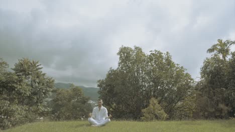 young man in white dress doing yoga meditation and spiritual movements in a beautiful green landscape mindfulness and tai chi