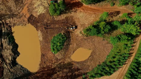 aerial drone top down shot over yellow excavator truck leveling land after deforestation during daytime