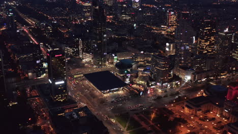 Night-aerial-panoramic-footage-of-city-centre-with-square,-train-station-building-and-Zlote-Tarasy-modern-shopping-and-entertainment-complex.-Warsaw,-Poland