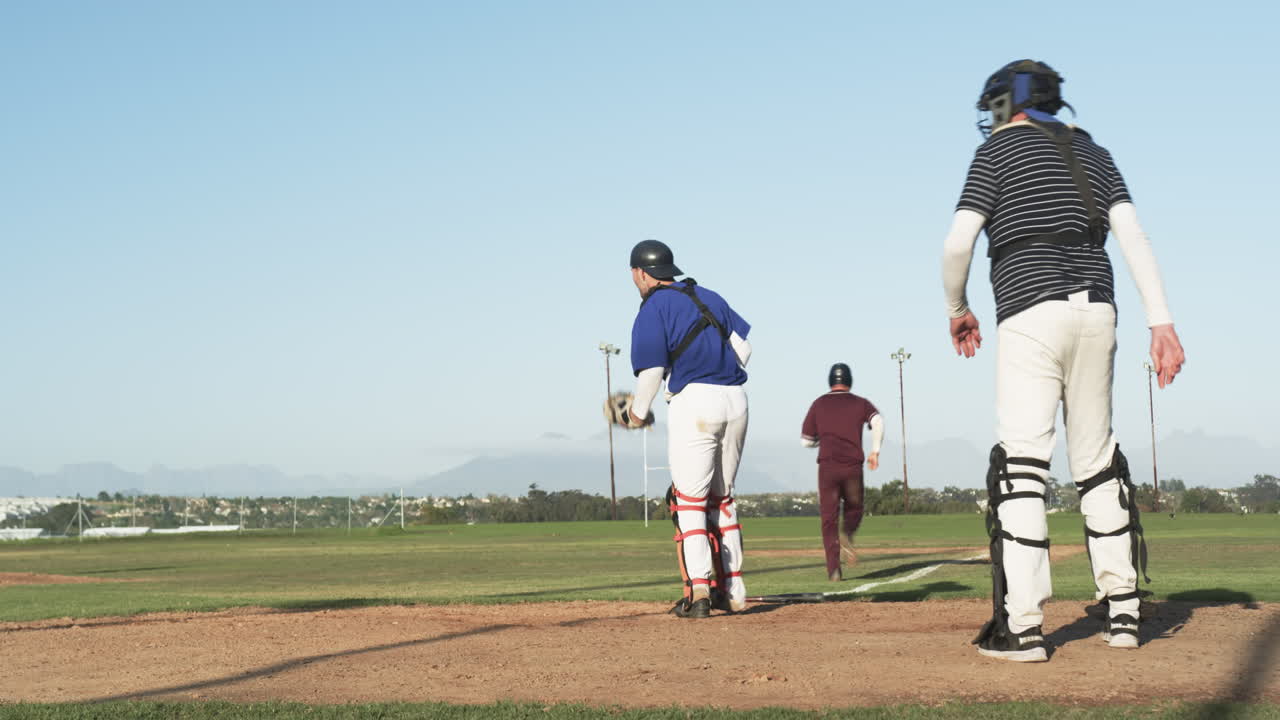 Giocando a baseball, un ricevitore salta per prendere la palla mentre un corridore scivola verso la base.