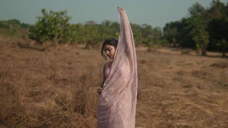 Mujer-Con-Sari-Rosa-Parada-En-Un-Campo-De-Hierba-Seca-Con-Un-Paño-Sobre-La-Cabeza,-Humor-Sereno,-Durante-El-Día