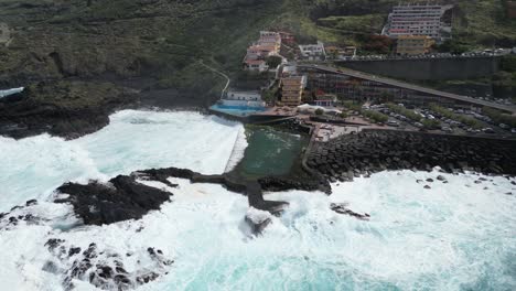 strong ocean waves hitting mesa del mar natural sea water pool in tenerife canary islands spain, aerial dolly left shot