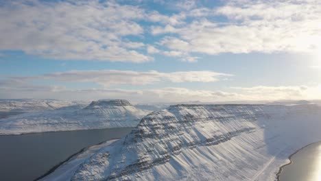 Drone-flying-over-Bright-white-snowy-mountains-of-the-Westfjords,-Iceland-in-the-sun-in-arctic-sea---aerial-flight