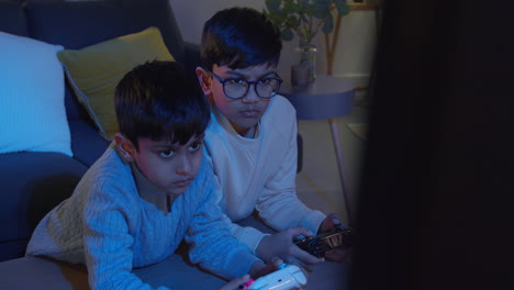 Dos-Niños-Pequeños-En-Casa-Jugando-Con-Una-Consola-De-Juegos-De-Computadora-En-La-Televisión-Sosteniendo-Controladores-A-Altas-Horas-De-La-Noche-2