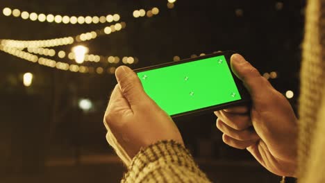 handheld camera: point of view of man at using phone with green mock-up screen chroma key surfing internet watching content videos blogs tapping on center screen