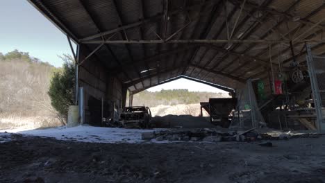 Slider-Footage-Under-an-Abandoned-Covered-Storage,-With-Decaying-Machinery-and-a-Vandalized-Car-in-the-Winter-with-Snow