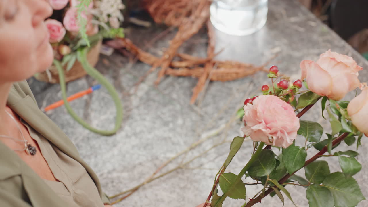 Caucasian florist final touches on bouquet, close portrait inspection of berries and roses, gentle adjustment of stems and leaves, warm ambient studio light, focused artisan expression