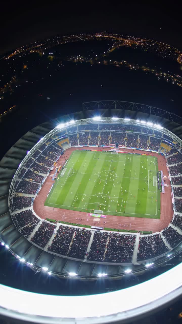 Aerial video shot of a brightly lit stadium at night, showcasing a football match with a wide-angle