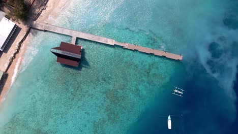 epic aerial top down of crystal clear coral reefs under wooden pier on gili meno island during sunshine