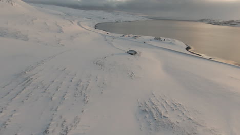 Winter-scenery-with-farm-by-fjord-at-sunset-and-mountain-background,-Iceland