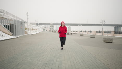 athlete jogging on interlocked pavement outdoors in winter, surrounded by snow-covered ground, modern urban structures like a bridge, lamp posts, benches, and serene cold-weather scenery