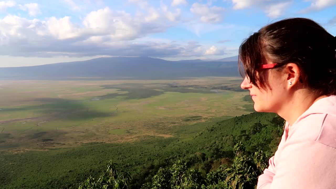mujer con anteojos gira la cabeza sonriendo con el paisaje volcánico de ngorongoro en segundo plano