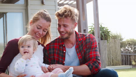 happy white couple and young daughter sitting outside house