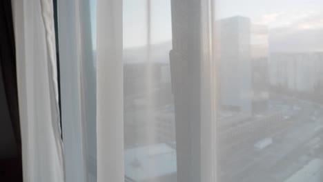 a view of a cityscape from a window with white curtains