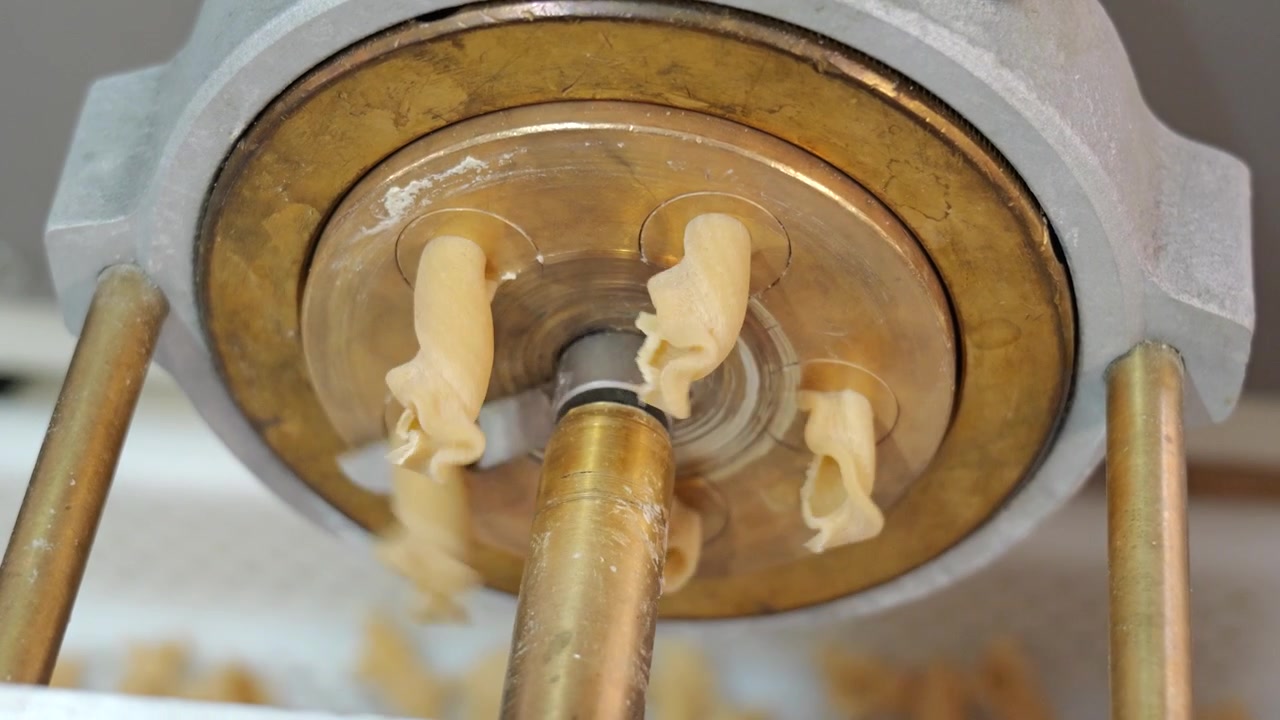 Primo piano dal basso di impasto fresco per pasta che fuoriesce da una macchina e viene tagliato durante la produzione artigianale di pasta.
