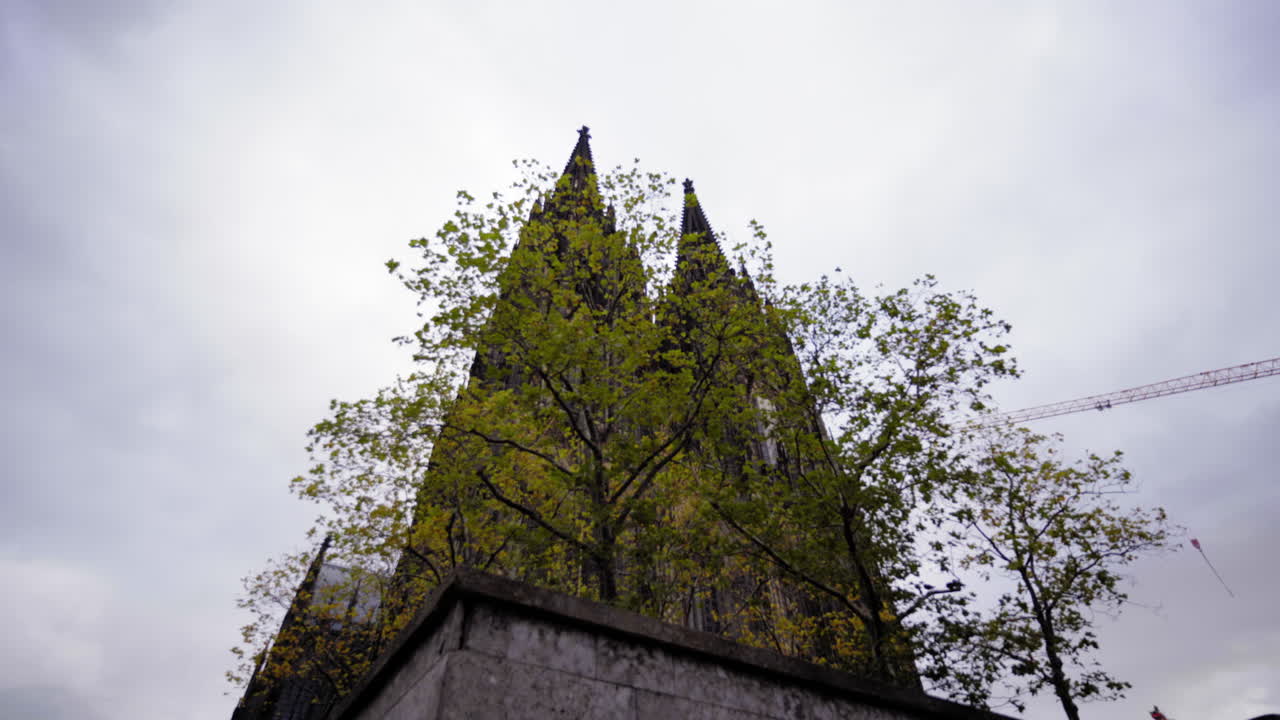 The iconic Cologne Cathedral spires partially hidden by vibrant autumn foliage, highlighting the interplay between nature and historic architecture in Cologne, Germany