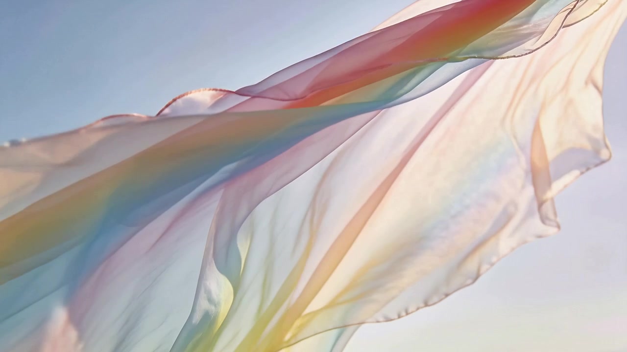 Sciarpa arcobaleno traslucida che ondeggia dolcemente alla leggera brezza, fluttuando in un cielo azzurro pallido e soleggiato.