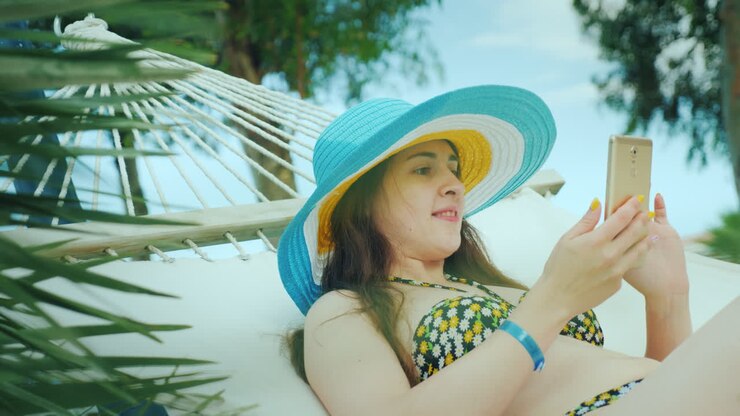 Una giovane ragazza dai capelli scuri in bikini e con un cappello a tesa larga e luminoso si riposa su un'amaca.