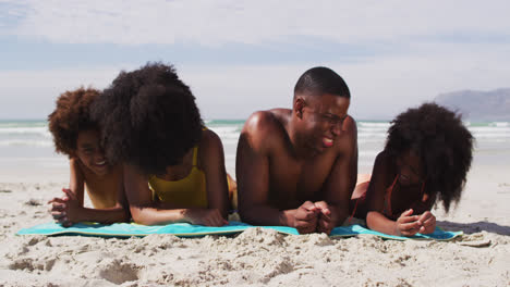 Retrato-De-Padres-Afroamericanos-Y-Dos-Niños-Tumbados-Sobre-Una-Toalla-En-La-Playa-Sonriendo