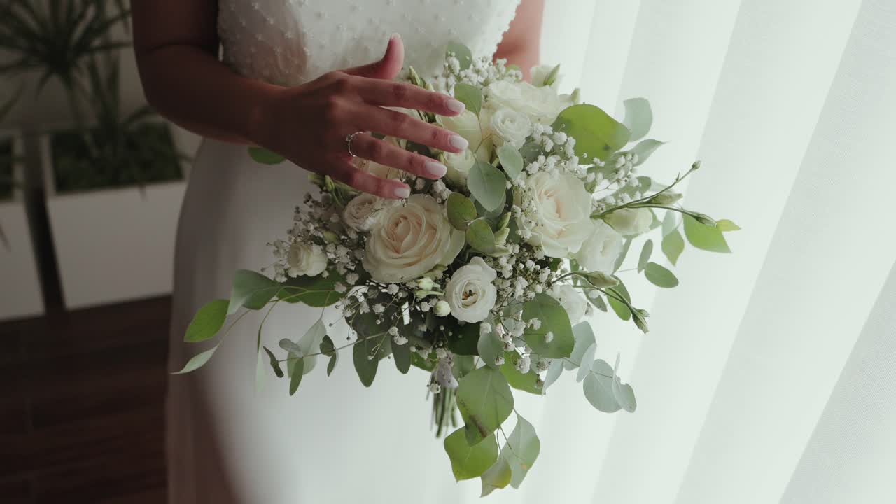 Primo piano di una sposa che tiene un bouquet con rose bianche, gypsophila e foglie verdi
