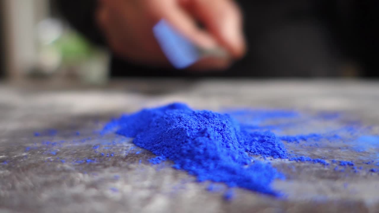 Atölyede bir masada mavi toz pigment hazırlayan sanatçının yakın çekimi.