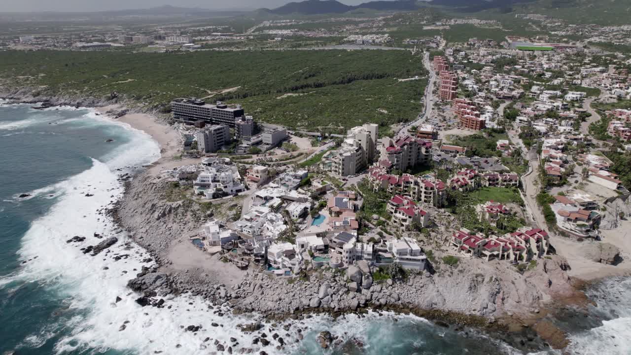 drone volando sobre múltiples resorts y casas junto a la playa en cabo san lucas