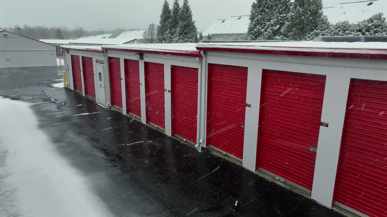 Letecký pohled na sněhovou bouři nad červenými garážemi v průmyslové čtvrti amerického města. Mokrá ulice v zimním období. Budovy samoobslužných skladů v červených barvách.